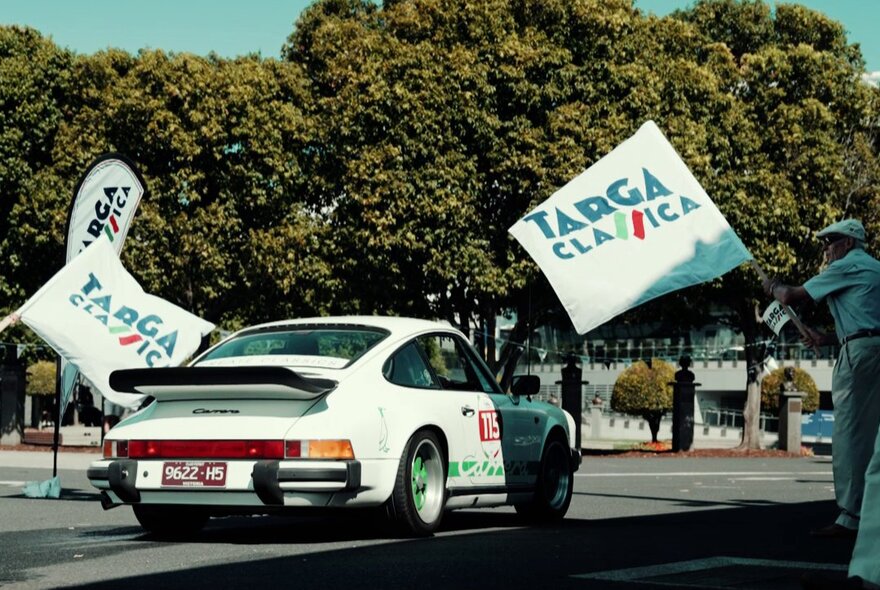 Vintage Porsche driving between flags with trees.