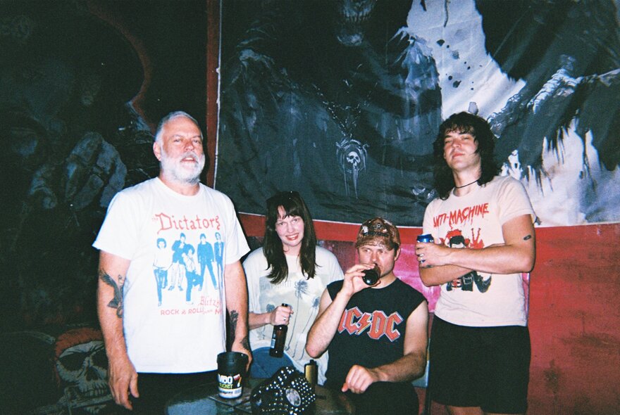 A photo of four people posing for a picture in a dimly lit room with abstract art on the wall.