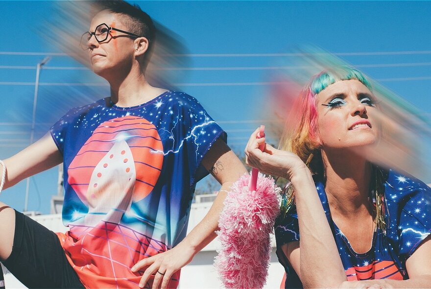 Two people in matching futuristic tshirts with blurring around their head, one of them holding a pink feather duster. 