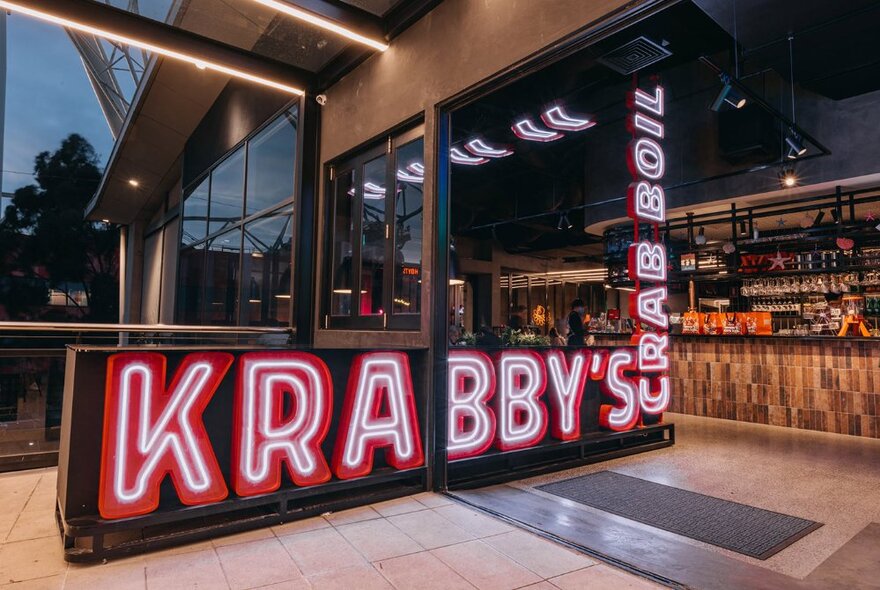 Red and white neon signage next to restaurant bar counter and windows.