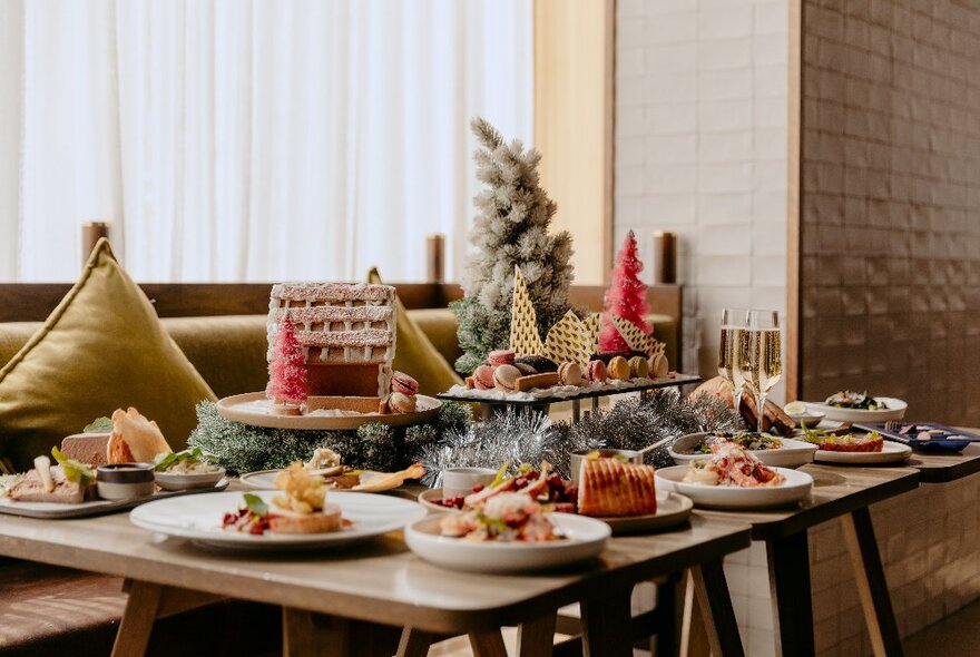 A table at a restaurant filled with plates of Christmas themed food, including a gingerbread house, and a festive centrepiece.