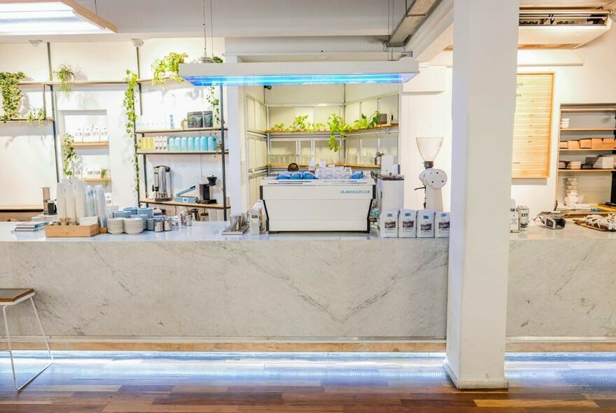 Poolhouse Coffee interior with white marble bench topped with coffee machine, cups and coffee-making items, with shelves on white wall behind.