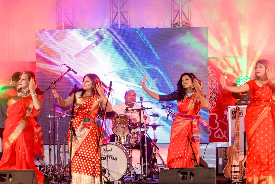 A group of traditional Indian dancers wearing red saris are performing on stage
