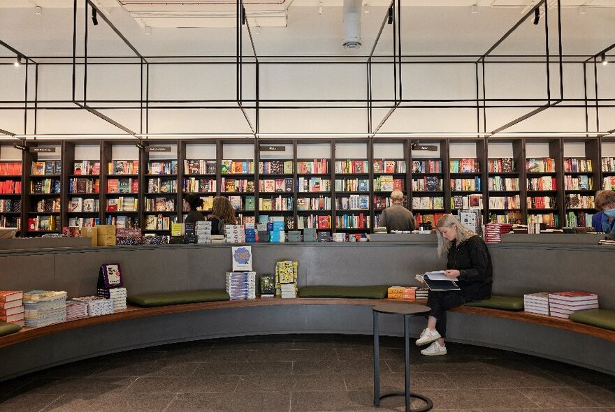 Curved couch with a seated person flicking through a book, with many shelves of books against the rear wall.