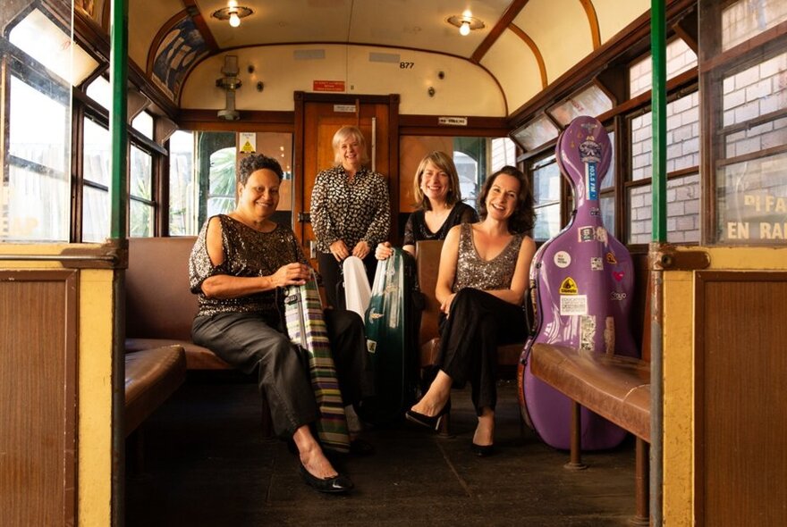 The four members of the Flinders Quartet seated with their instruments in cases beside them, inside a stationary vintage W class Melbourne tram.