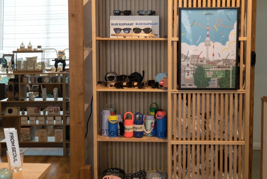 A wooden shelf in a shop, displaying items such as sunglasses, drink bottles and a poster.