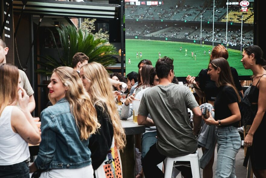 Patrons inside Melbourne Public, drinking and watching sport on a large television screen.