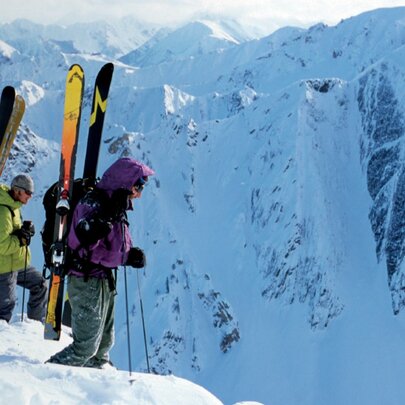People standing on an icy precipice with snow skies on their backs.