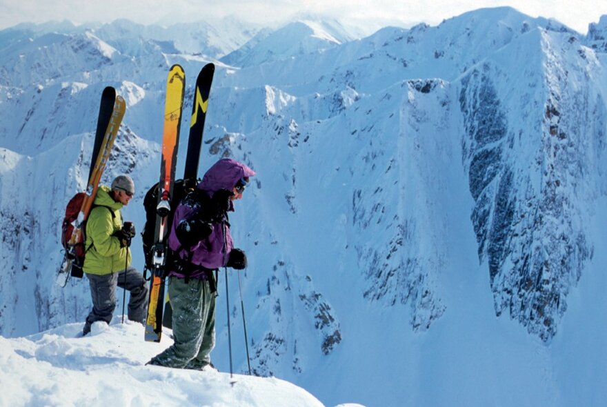 People standing on an icy precipice with snow skies on their backs.