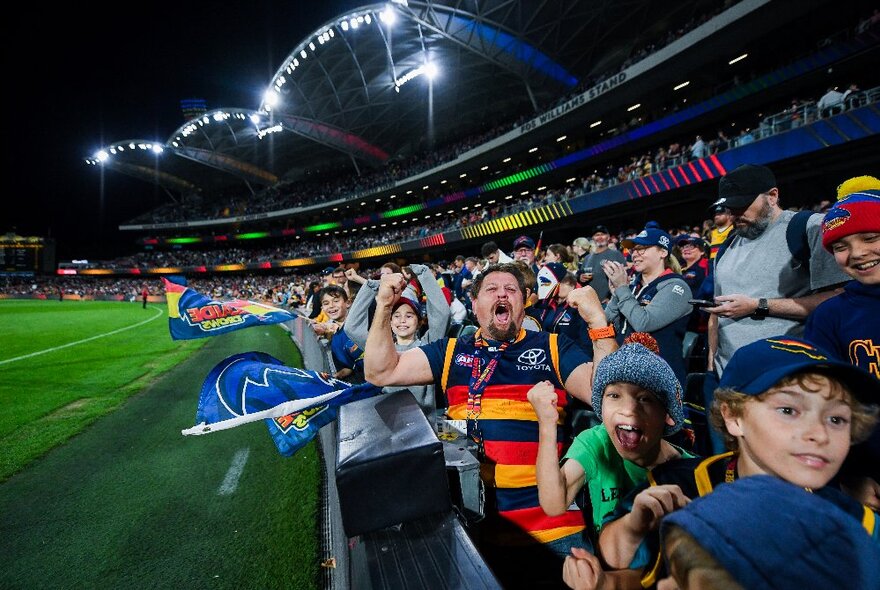 A footy crowd at the fence next to the oval of a large football stadium.