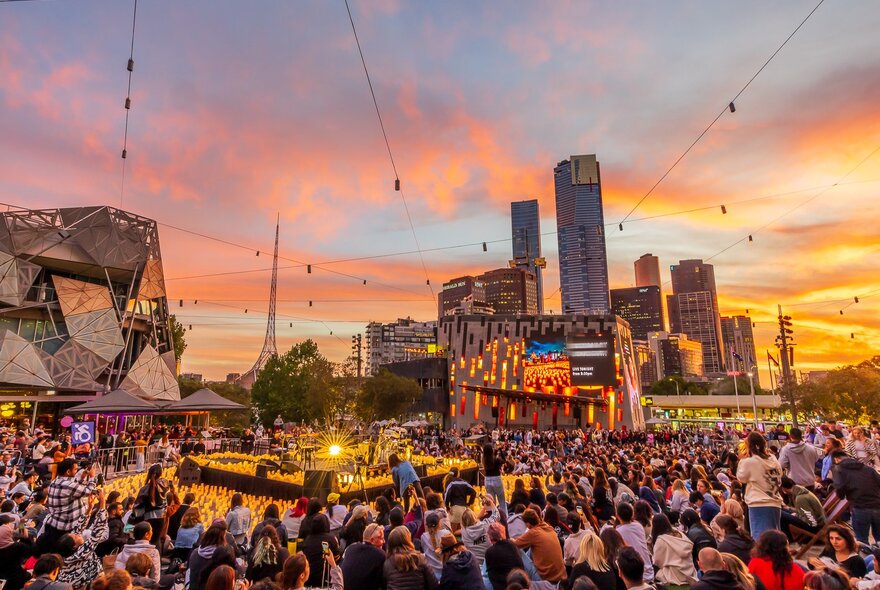 A performer surrounded by candles and crowds in the city at sunset.