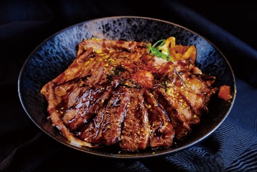 Bowl of sliced beef on a bed of rice with a garnish.