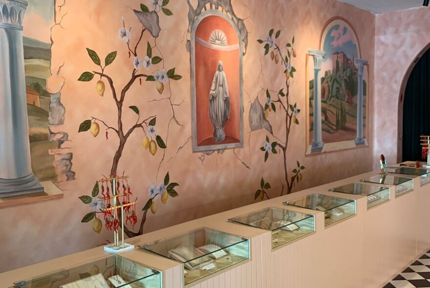 Jewellery store interior with walls frescoed with plants and niche statue, counter with glass-topped display cases.