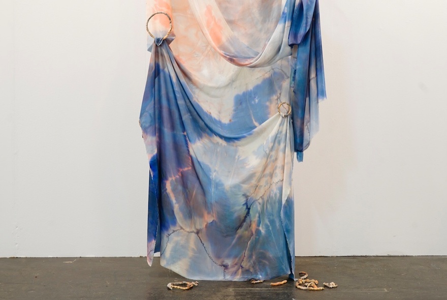 A draped, pastel-swirled blue and peach silk piece of fabric hanging from a gallery wall.