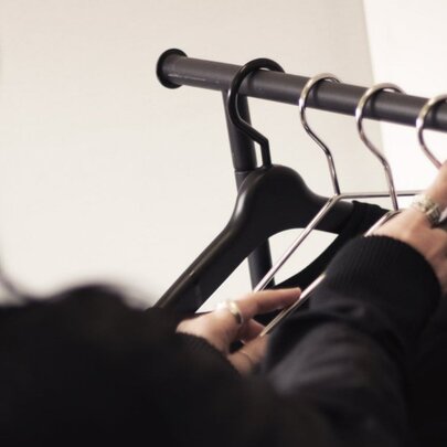 A hand reaching towards hangers on a clothing rack.