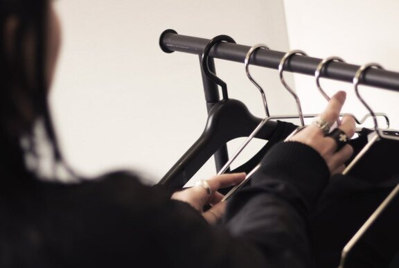 A hand reaching towards hangers on a clothing rack.