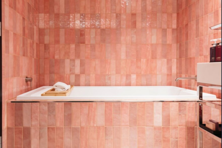 A bathroom at Quincy Hotel Melbourne with pink tiled walls and insert white bathtub.