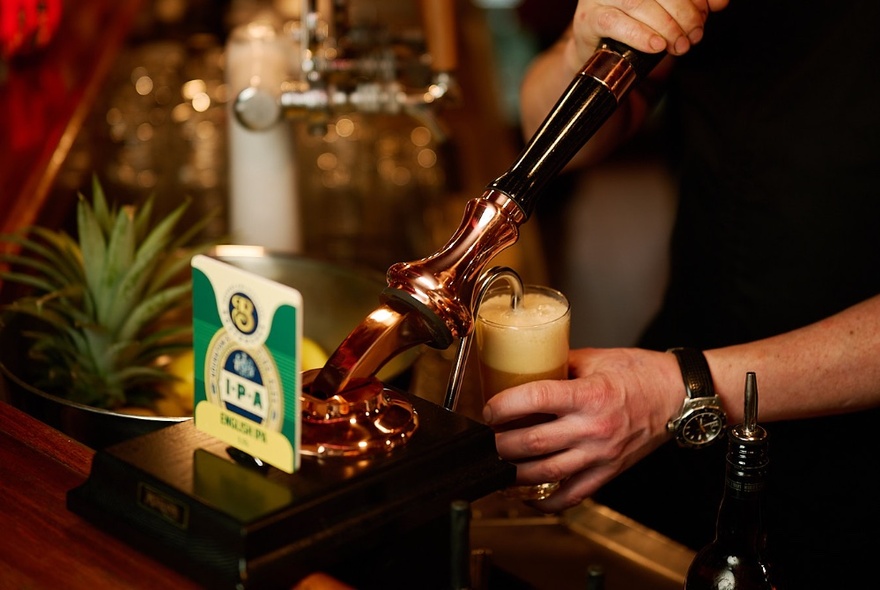 A bartender pouring a beer from an old-style brass beer tap.