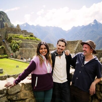 Three smiling friends standing at a lookout with the ruins of Machu Pichu  behind them.