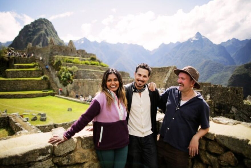 Three smiling friends standing at a lookout with the ruins of Machu Pichu  behind them.