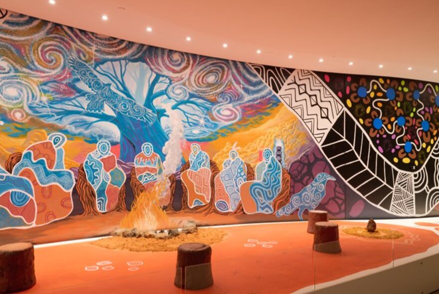 A gallery space featuring an indigenous mural artwork on the wall.