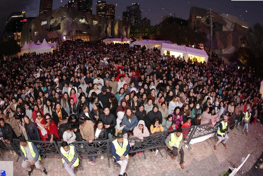 A crowd of people at Federation Square at night, all faced towards the main stage.