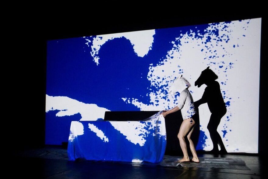 Musician wearing an animal head mask performing on stage against a blue and white art lightshow.