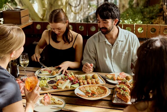 Four people enjoying a full table of brunch plates at an ourdoor restaurant.