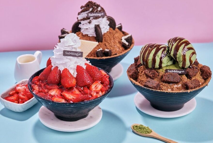 Three bingsu bowls with chocolate being drizzled on top. One is choc mint, one is cookies and cream the other is strawberry. 