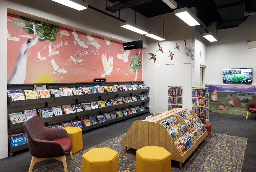 The children's reading area at City Library with low shelves of books, rugs and small stools, and colourful artwork on the walls.