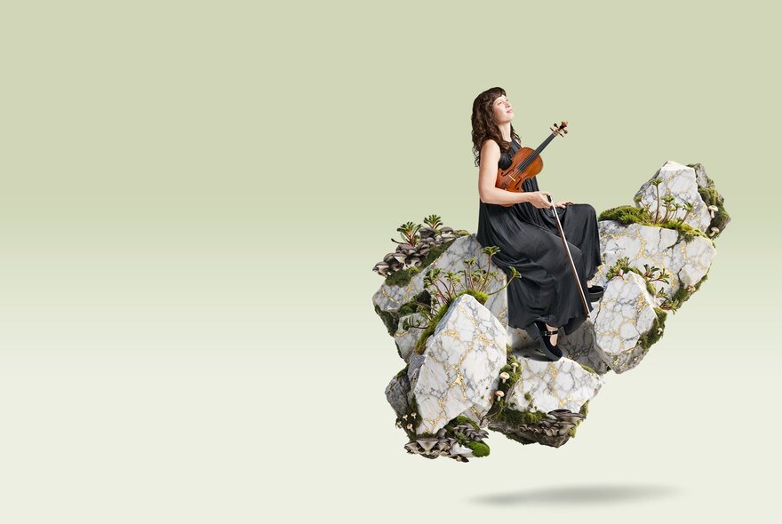 A violinist dressed in a black dress, holding their violin under their arm, seated on a floating, textured rock formation adorned with small plants, against a light coloured background.
