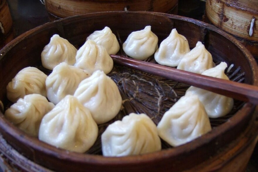 Dark basket of xialong bao dumplings, with chopsticks.