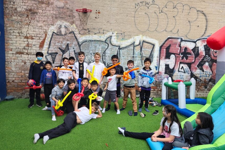 An outdoor area with a bouncy castle and lots of kids holding up balloon animals. 