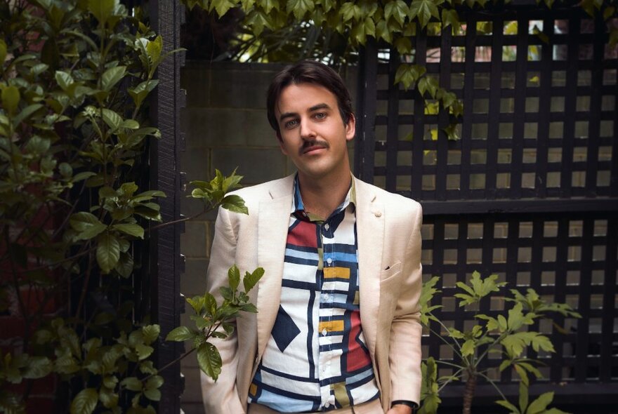 Sweeney Preston wearing a white suit jacket posing in an outdoor courtyard garden.