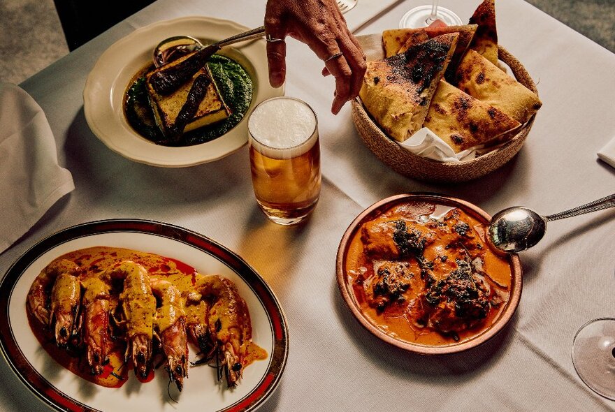 A table with curries, prawns, nan bread and beer on it. 