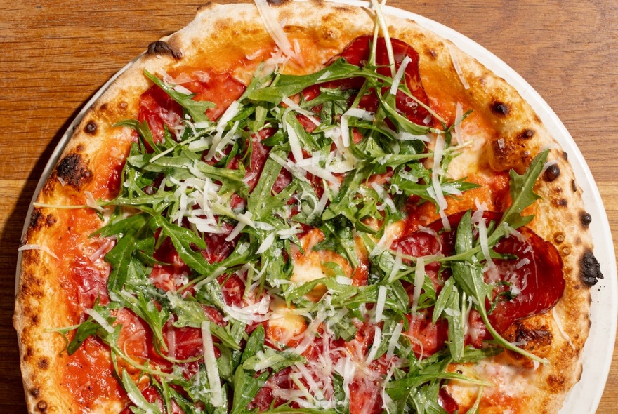 A traditional-looking Italian pizza with tomato, rocket and grated mozzarella.