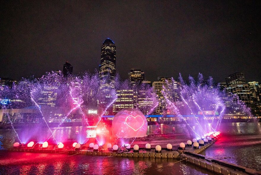 A river light show with pink lights and a giant orb showing a heart image.