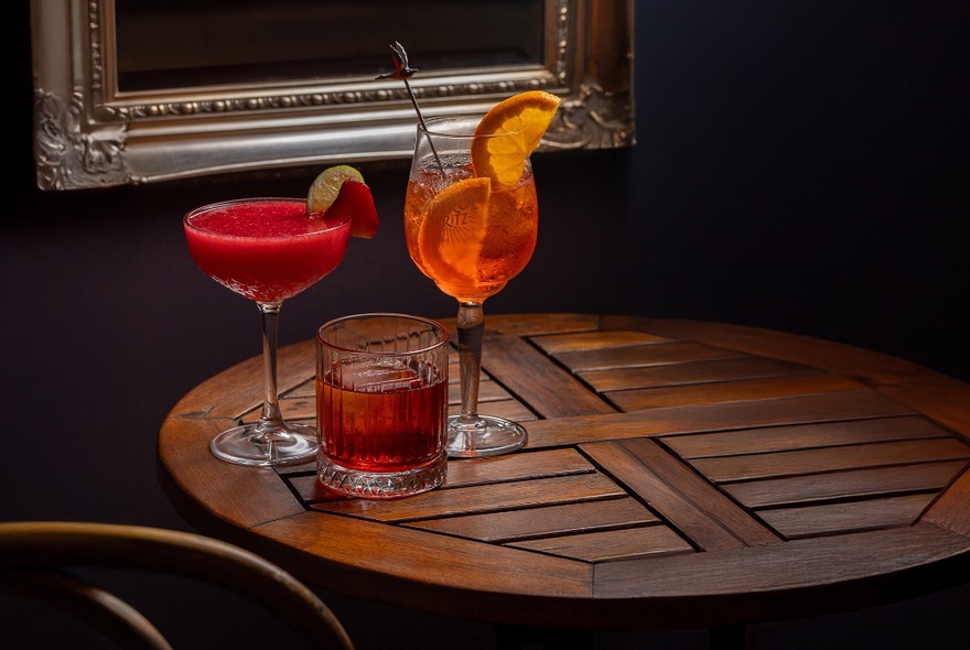 Three cocktails on a wooden table, inside a room.