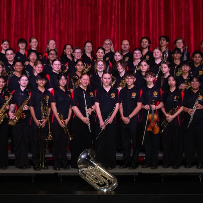 La Salle College Concert Band assembled for a group shot on stage in front of a red curtain. 
