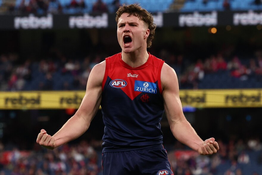 A Melbourne football player celebrates with arms outstretched. 
