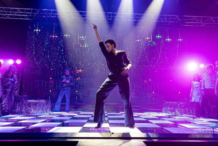 A classic solo pose  with a hand in the air from a performer in the musical Saturday Night Fever. 