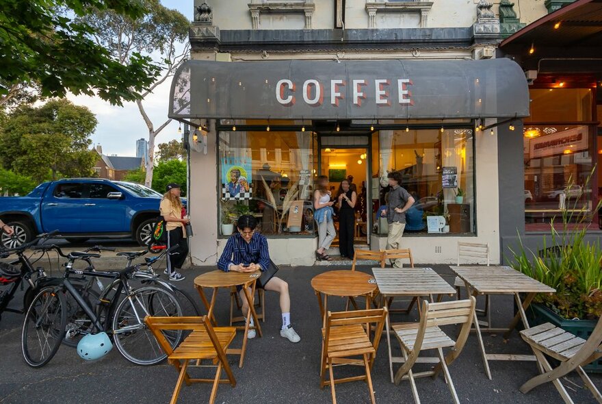 People hanging out outside a small coffee shop with tables outside.