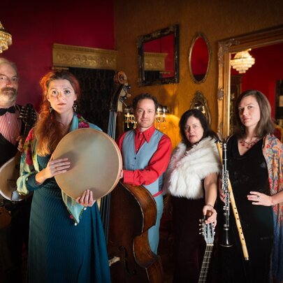 Costumed performers in a bohemian lounge setting with instruments, candelabra and mirrors.