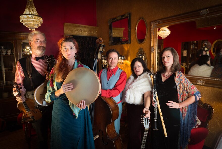 Costumed performers in a bohemian lounge setting with instruments, candelabra and mirrors.