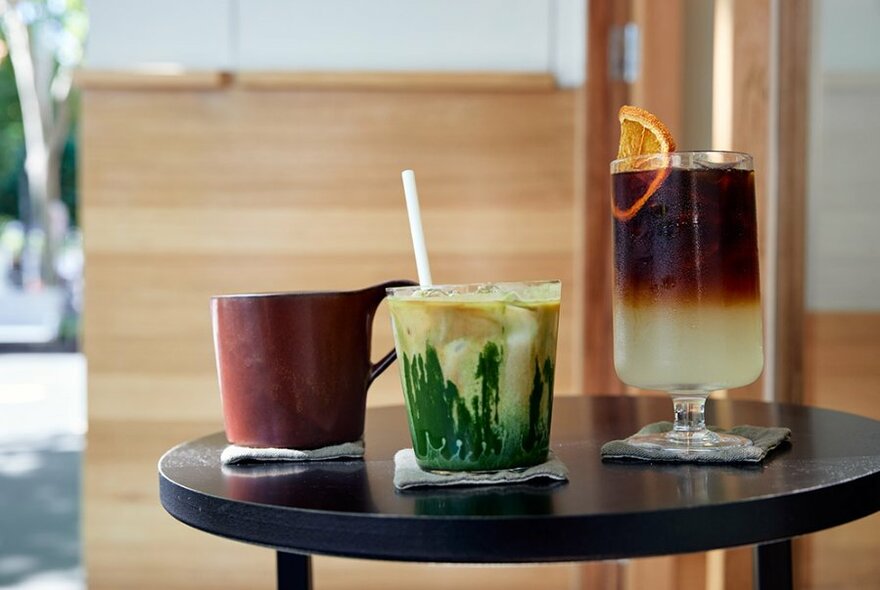 Three drinks on a small table, including a matcha latte.