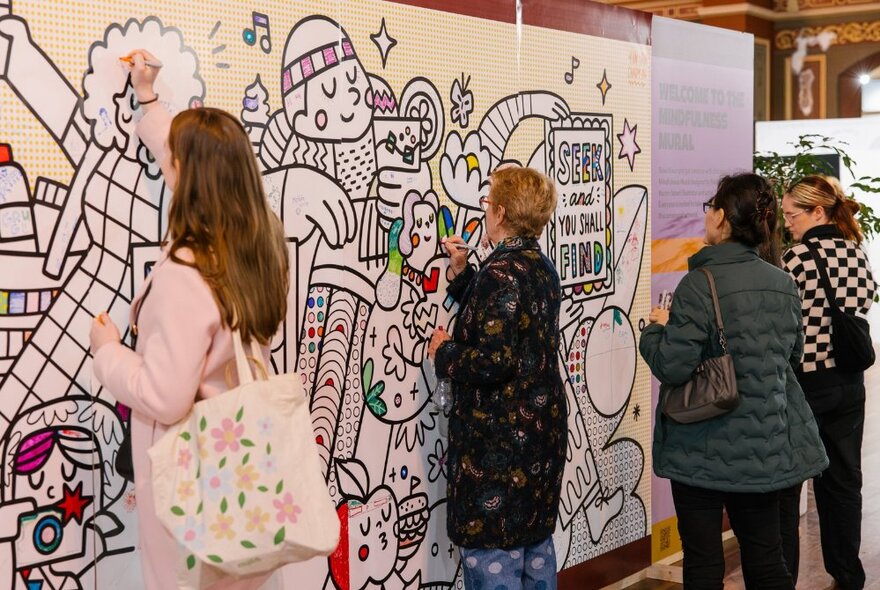 Shoppers at a design market colouring in a large wall mural.