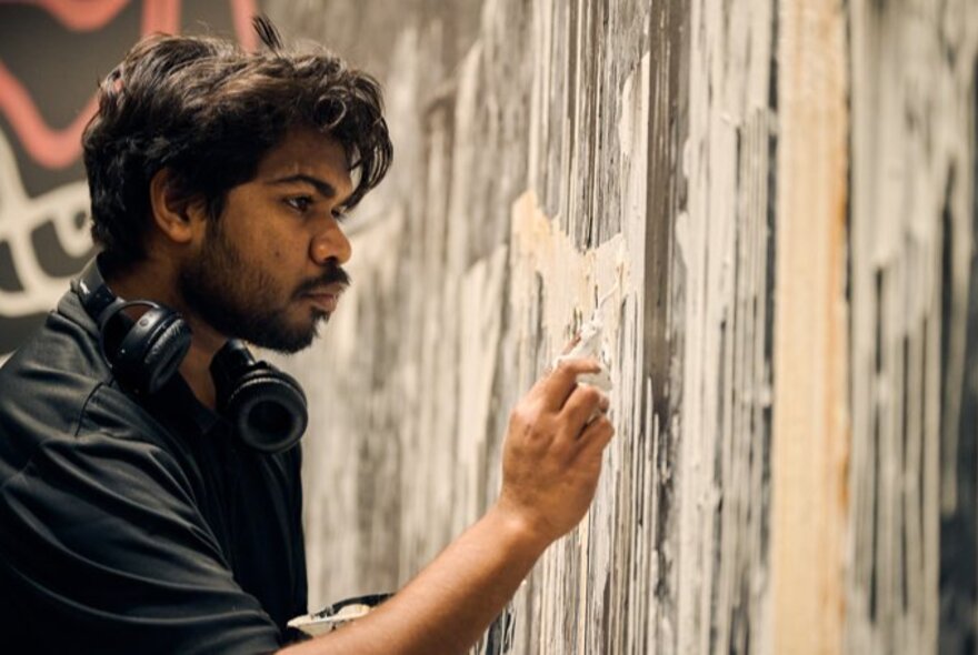 An Indigenous man painting a mural with his hands.