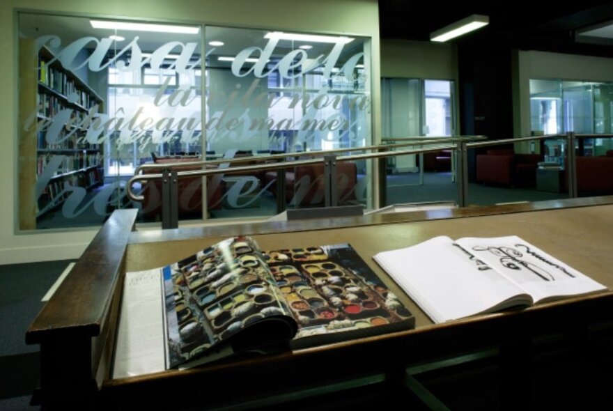 Interior of the City Library with large picture books opened on a desk and a room with lettering on the glass walls.