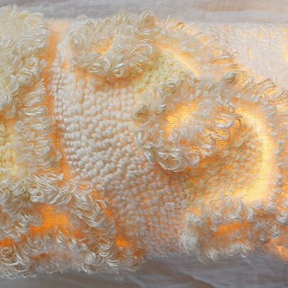 An illuminated textile sculpture in white / cream with a yellow glow. 