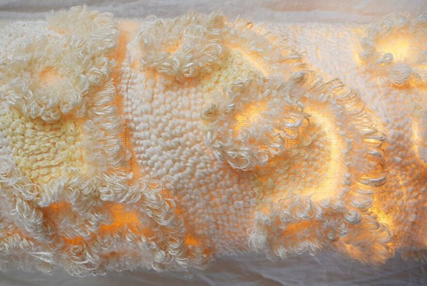 An illuminated textile sculpture in white / cream with a yellow glow. 